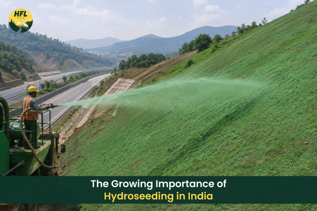 A worker uses hydroseeding equipment to spray green seed mixture onto a steep hillside beside a highway in a mountainous landscape.